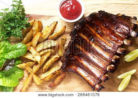 Homemade Baked Meat Ribs Served With French Fries, Herbs, Lime And Ketchup On A Wooden Board. Rustic
