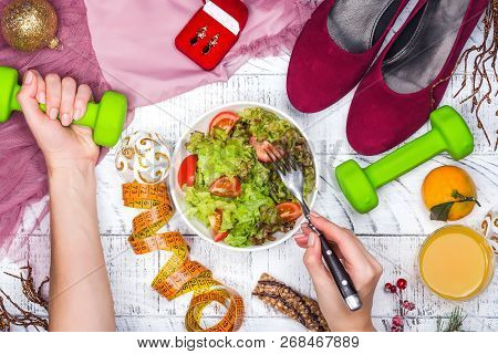 Woman Is Holding Dumpbell And Eating Fresh Healthy Salad Before Christmas Holiday For Becoming Fit. 