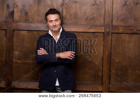 Calm Attractive Dark Haired Man In Elegant Suit Looking At You While Leaning On The Wooden Wall And 