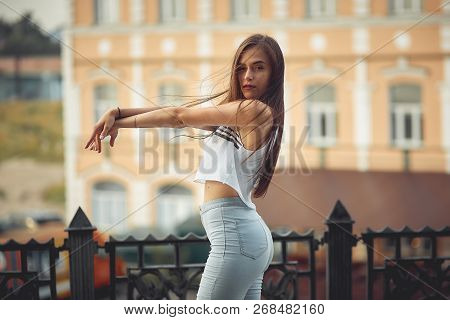 Portrait Of A Girl In Jeans And A T-shirt On The Background Of The Building In The Evening On A Summ
