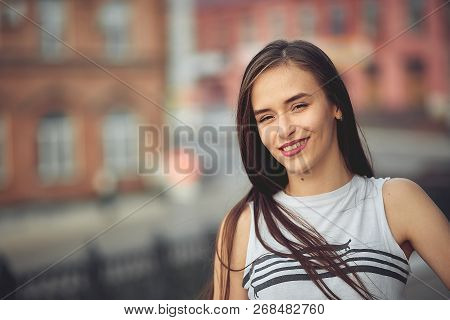 Portrait Of A Girl In Jeans And A T-shirt On The Background Of The Building In The Evening On A Summ