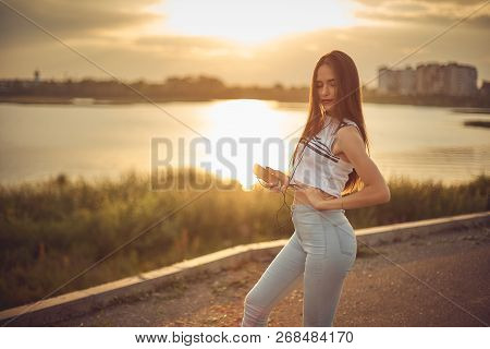 Young Beautiful Caucasian Girl Listening To Music With Smartphone Walking In The City With Headphone
