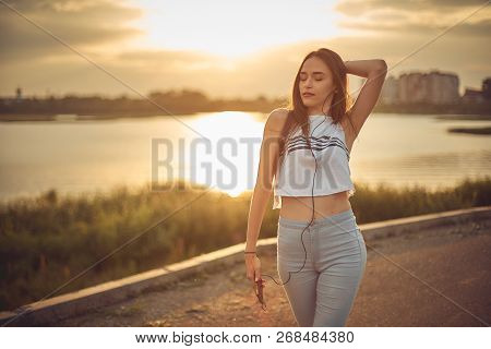 Young Beautiful Caucasian Girl Listening To Music With Smartphone Walking In The City With Headphone