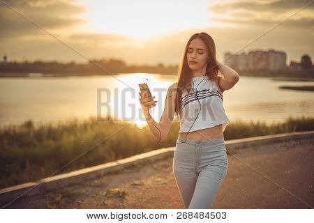 Young Beautiful Caucasian Girl Listening To Music With Smartphone Walking In The City With Headphone
