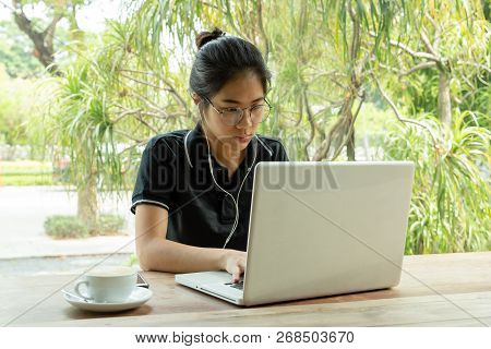 Young Asian Woman Student Working On Laptop With Earphone In Cafe.