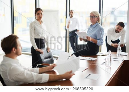 Female economists looking at one of colleagues while discussing financial papers at meeting