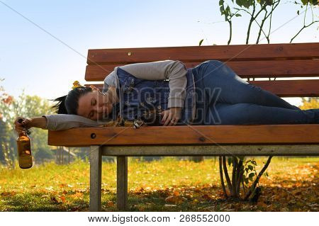 A Drunk Young Woman Sleeping On A Bench In The Day.a Young Woman Holding A Bottle Of Alcohol In Her 