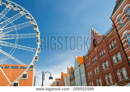 Big Ferris Wheel, Traditional Typical Orange Buildings On Pedestrian Stagiewna Street With Blue Sky 