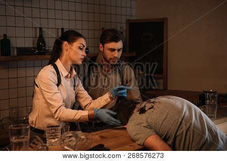 Concentated Female And Male Detectives Collecting Evidence From Dead Body And Investigating Crime Sc