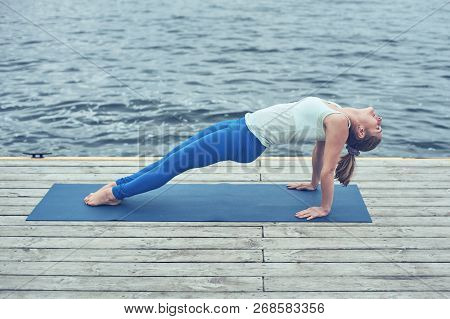 Beautiful Young Woman Practices Yoga Asana Purvottanasana Upward Plank Pose On The Wooden Deck Near 