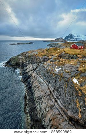 Clif with traditional red rorbu house on Litl-Toppoya islet on Lofoten Islands, Norway in winter