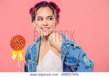 Pretty pink-haired girl with lollipop in denim jacket posing on a pink background. Fashion, beauty. Youth style of clothes.