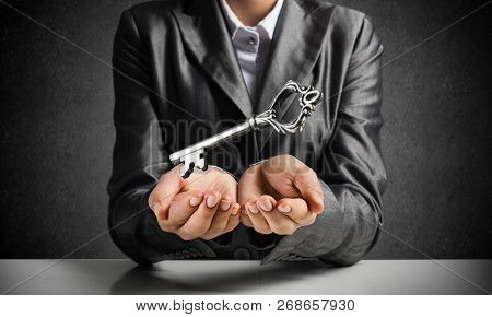 Cropped Image Of Businessman In Suit Keeping Big Key In Hands With Dark Wall On Background.
