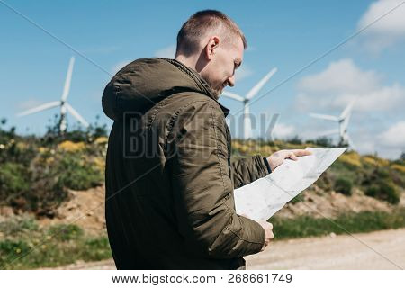 A Tourist Man Looks At The Map Of The Area For Further Travel. Unknown Terrain Or Unfamiliar Territo
