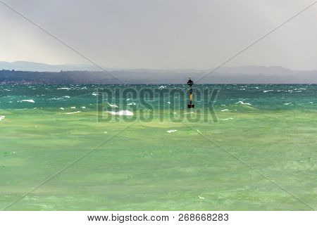 Black And Yellow Buoy In Turbulent Blue Green Waves On Lago Di Garda Lake, Windy, Cloudy, Foggy Weat