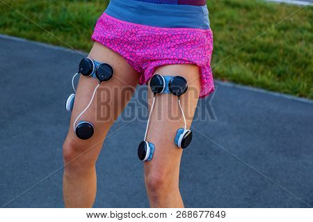 The Girl Is Engaged In Fitness With An Electrostimulator. Exercises And Load On The Leg Muscles With