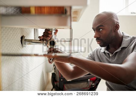 Young black male plumber sitting on the floor fixing a bathroom sink, close up