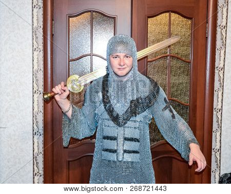 A Man Dressed Up In A Knights Hauberk At Home In His Room. Knights Sword In The Hands Of A Man. Knig