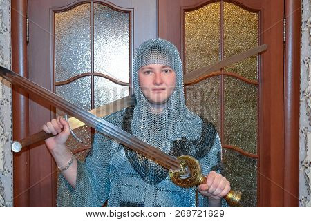 A Man Dressed Up In A Knights Hauberk At Home In His Room. Knights Sword In The Hands Of A Man. Knig