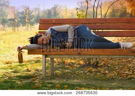A Drunk Young Woman Sleeping On A Bench In The Day.a Young Woman Holding A Bottle Of Alcohol In Her 