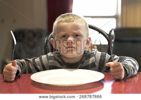 A Upset Little Boy Waiting For Dinner While Holding A Fork And A Spoon