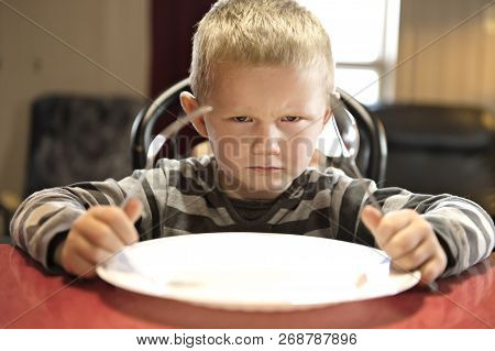A Upset Little Boy Waiting For Dinner While Holding A Fork And A Spoon