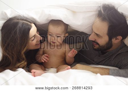 Couple Enjoying With Baby Under Blanket On Bed At Home