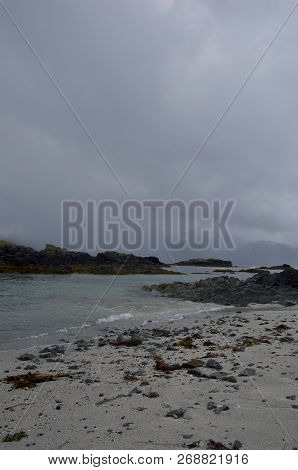 Grey Rain Clouds Hang Over Beach As Squall Hits Distant Mountains In Nuchatlitz Inlet, British Colum