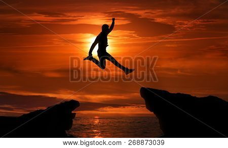 Freedom, Risk, Challenge And Success. Man Jumping Over Precipice Between Two Rocky Mountains At Suns