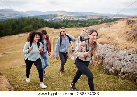 Multi ethnic group of five young adult friends hiking across a field uphill towards the summit, close up