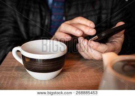 A Man Is Resting In A Cafe, Drinking Tea, Reading And Writing Messages On A Smartphone. Work In The 