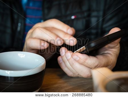 A Man Is Resting In A Cafe, Drinking Tea, Reading And Writing Messages On A Smartphone. Work In The 