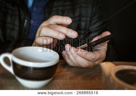 A Man Is Resting In A Cafe, Drinking Tea, Reading And Writing Messages On A Smartphone. Work In The 