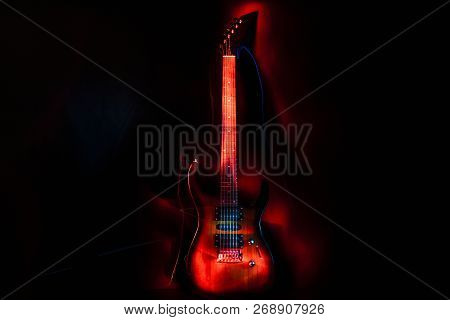Electric Guitar In The Rays Of Red On A Dark Background. Light Effect.