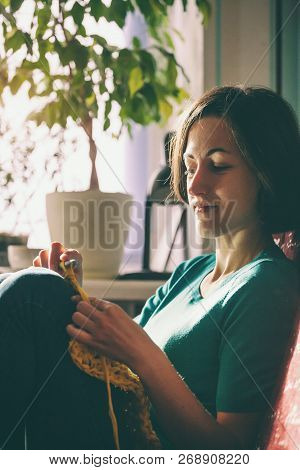Girl Knits Crochet At Home. Woman Engaged In Needlework. A Knitter Sits On A Sofa And Works. Creativ