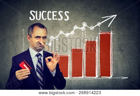 Financial Fraud Concept. Liar Dishonest Businessman Holding A Credit Card With Big Growing Pinocchio