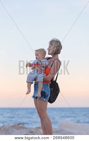Woman Playing With Her Baby Outside Against The Sea. The Concept Of A Happy Full-fledged Family Life