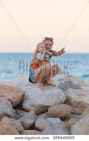 Woman Playing With Her Baby Outside Against The Sea. The Concept Of A Happy Full-fledged Family Life