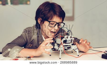 Boy Sitting At Desk And Constructing Robot At Home. Young Boy In Shirt. Indoor Joy. Modern Hobby Con