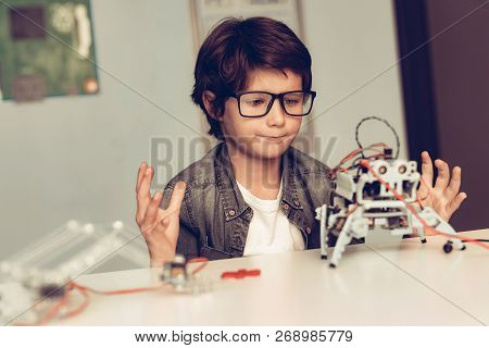 Boy Sitting At Desk And Constructing Robot At Home. Young Boy In Shirt. Indoor Joy. Modern Hobby Con
