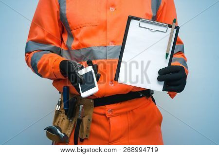 Building Contract. Fix List. Builder Is Holding Note Pad And Mobile Phone With Blank Screen In His H