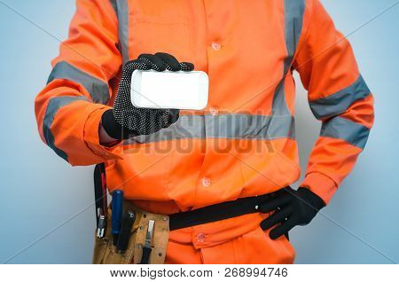 Builder Worker Is Holding In Hand A Blank Screen Mobile Phone. Call To A Repair Man Concept. Contact