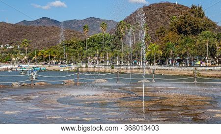 Jets Of Water From A Fountain Spraying The Ground On The Promenade Of Lake Chapala With The City In 