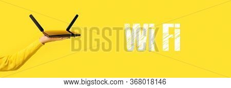 Black Wifi Router On Hand And Wifi Inscription Over Yellow Background, Panoramic Image