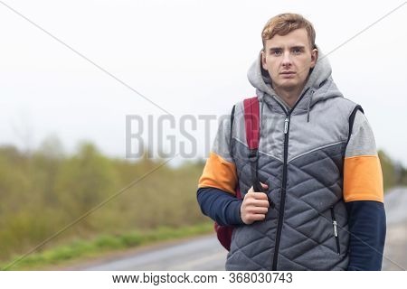 Tired Young Man Traveler With Backpack Trying To Stop, Catch Taxi Car, Cab. Guy Stands Near The Road