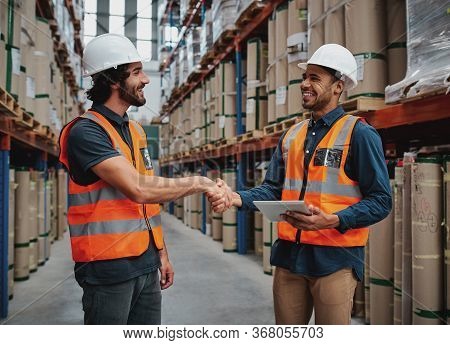 Two Cheerful Man Making A Firm Handshake In Logistics Workhouse Holding A Digital Tablet In Safety H