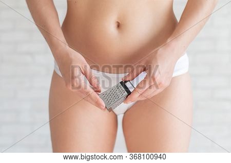 Unrecognizable Woman In White Panties Holds A Mini Grater. Metaphor Of The Bristles After Depilation
