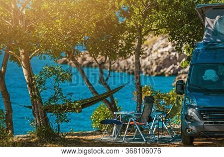 Scenic Outdoor Camping Spot. Motorhome, Garden Chairs And Hammock Between Trees. Sea Shore Scenery. 