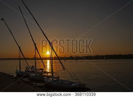 Traditional Egyptian Felluca River Boats Moored On The Nile River Bank With Sunset And Reflection In