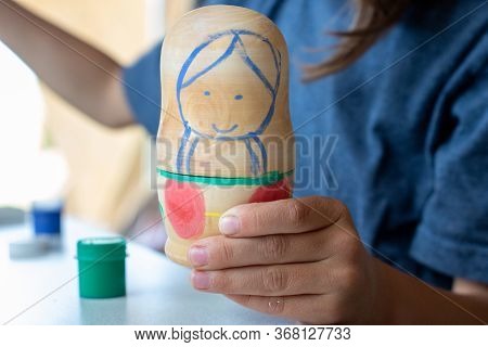 A Child Paints A Wooden Blank Of A Nesting Doll. Children's Crafts